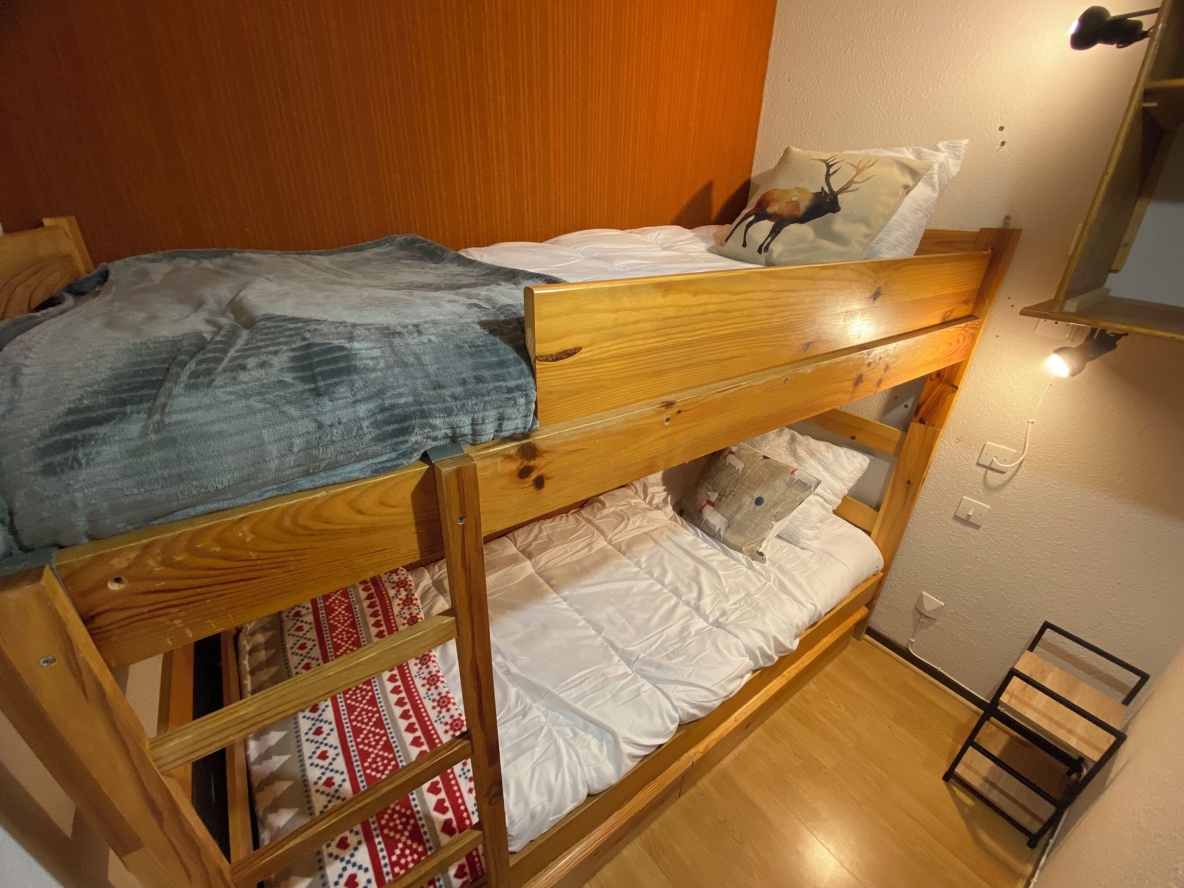Una cama litera con una manta azul, sábanas blancas y un cojín con diseño de ciervo.