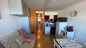 A compact living space with a kitchenette, a dining area, and a sofa with a patterned cover. - Apartment facing the mountains -la Belle étoile (Eyne)