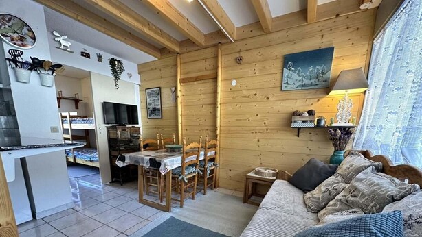 Een gezellig chaletinterieur met een eethoek, keuken en een woonkamer met een bank en vloerkleed.
