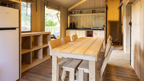 Un interno in legno con un tavolo da pranzo, sedie, un frigorifero e un angolo cottura dotato di scaffali e un piano di lavoro.