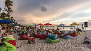 A beach with colorful bean bags and umbrellas, people relaxing, and a sunset in the background. -  D' Village Cottage 2 – Private Pool Villas (Langkawi)