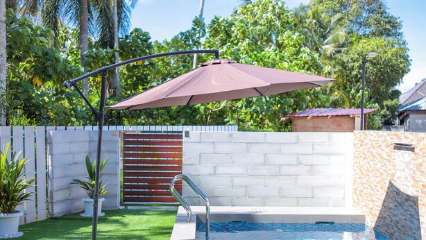 A swimming pool with a metal ladder, a metal umbrella, and a white brick wall. -  D' Village Cottage 2 – Private Pool Villas (Langkawi)