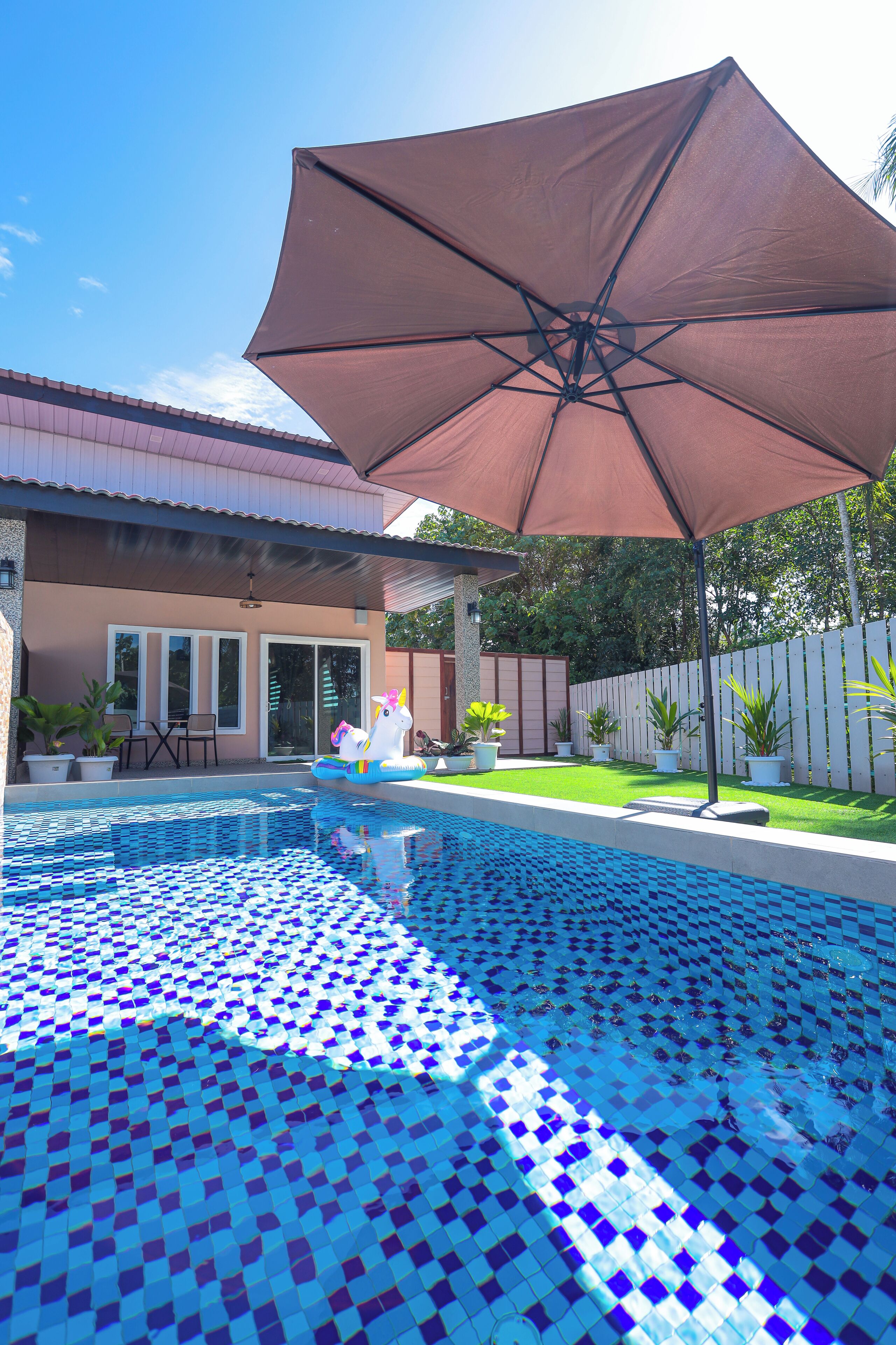 A swimming pool with a tiled floor, a large umbrella, and potted plants around the area.
