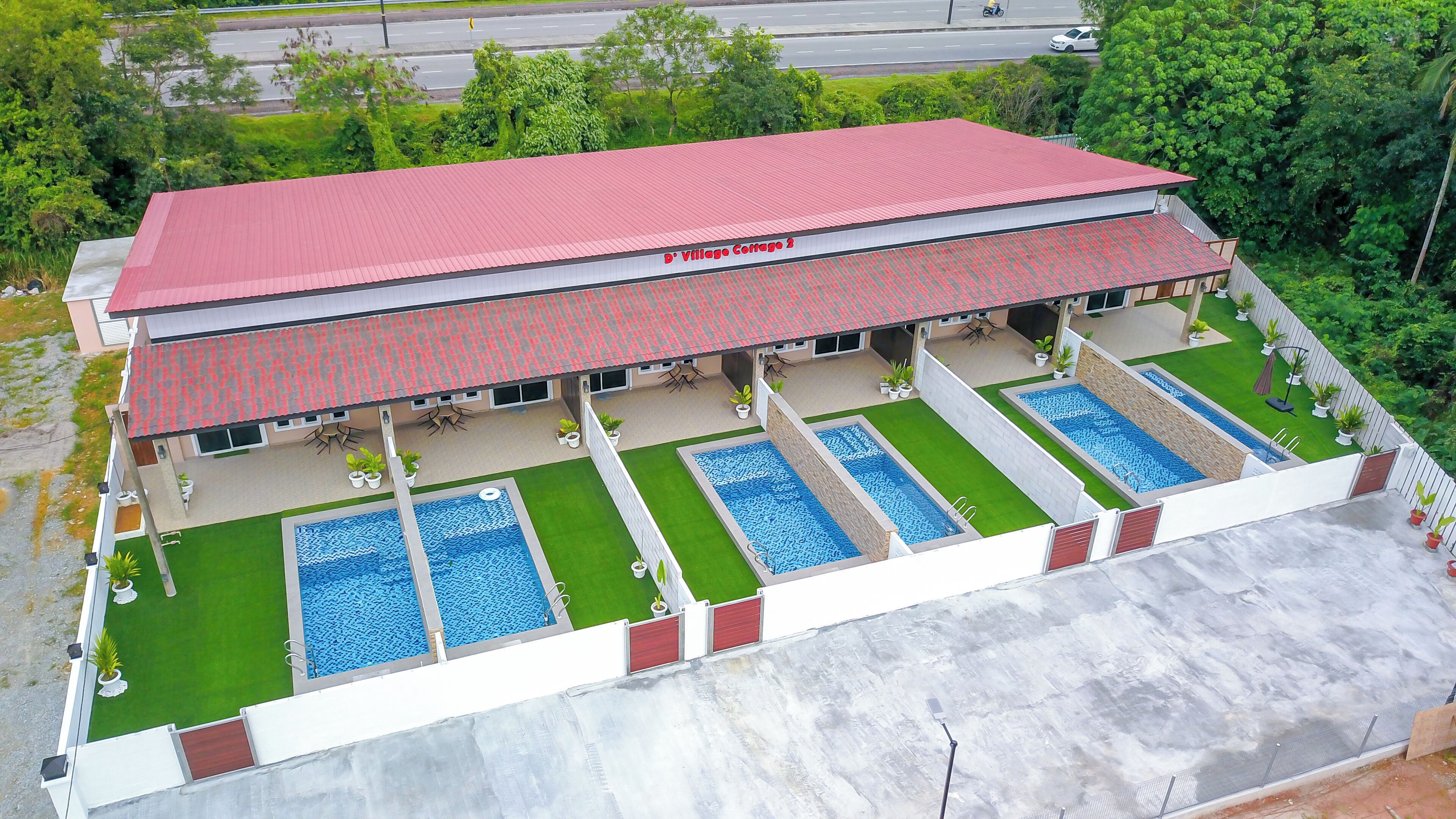 A two-story building with a red roof, labeled "D. Village Cottage 2," featuring a swimming pool area with four pools and a covered patio with outdoor seating.