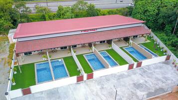 A two-story building with a red roof, labeled "D. Village Cottage 2," featuring a swimming pool area with four pools and a covered patio with outdoor seating.