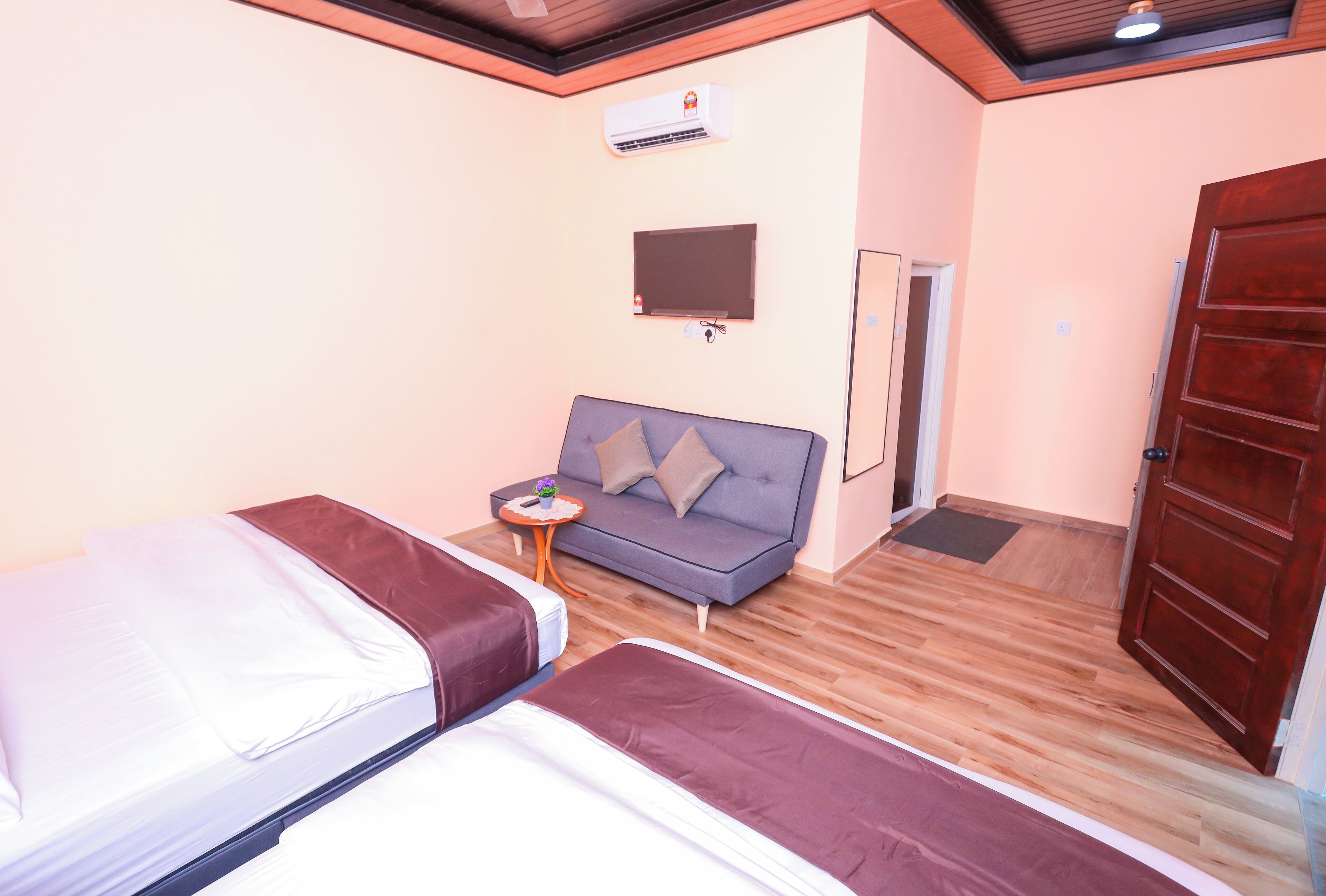 Une chambre d’hôtel avec deux lits, un canapé, une télévision, un climatiseur et un plancher en bois.