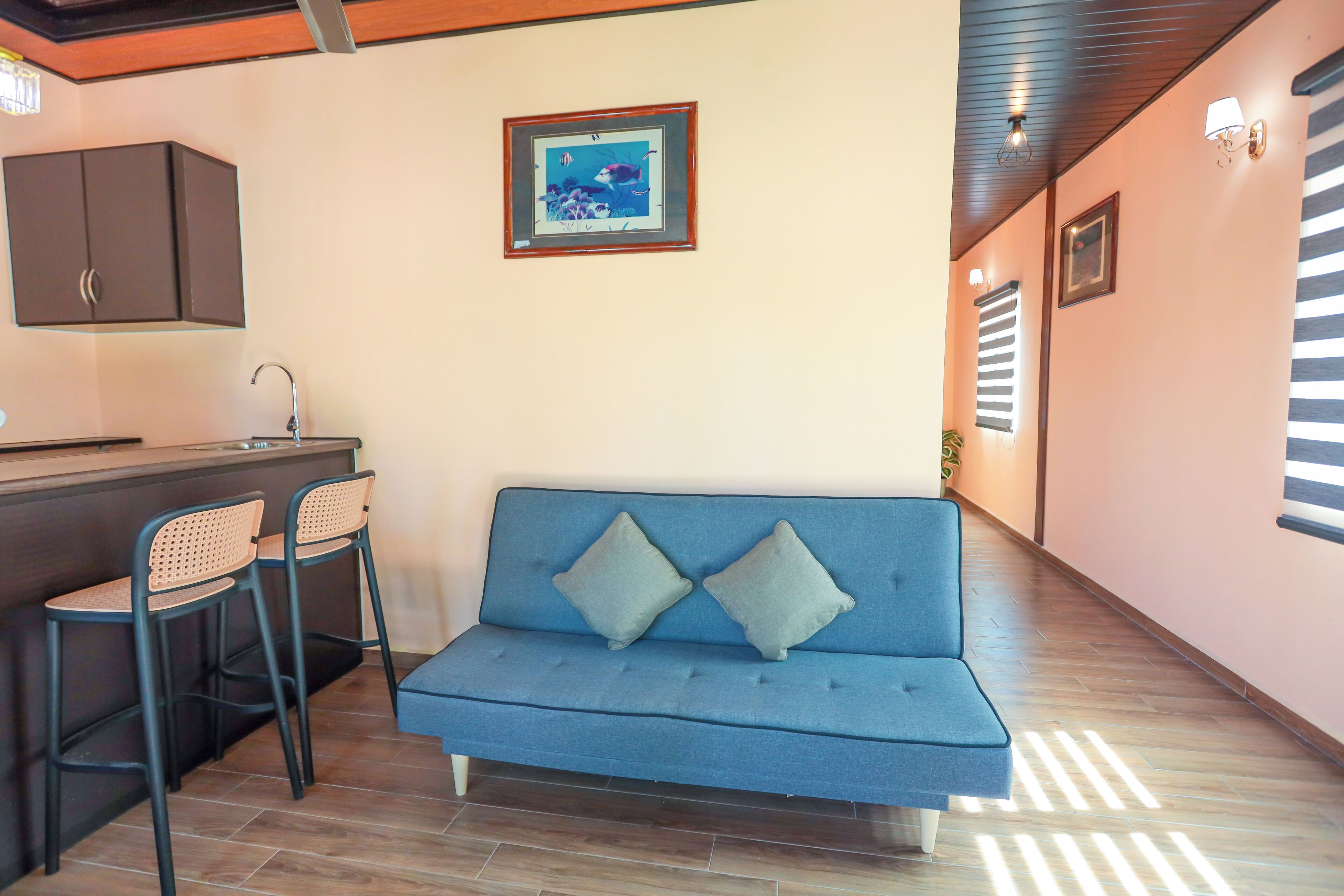 Ein blaues Sofa mit zwei Kissen, eine kleine Bar mit zwei Stühlen, ein gerahmtes Bild an der Wand und eine Holzzielung.