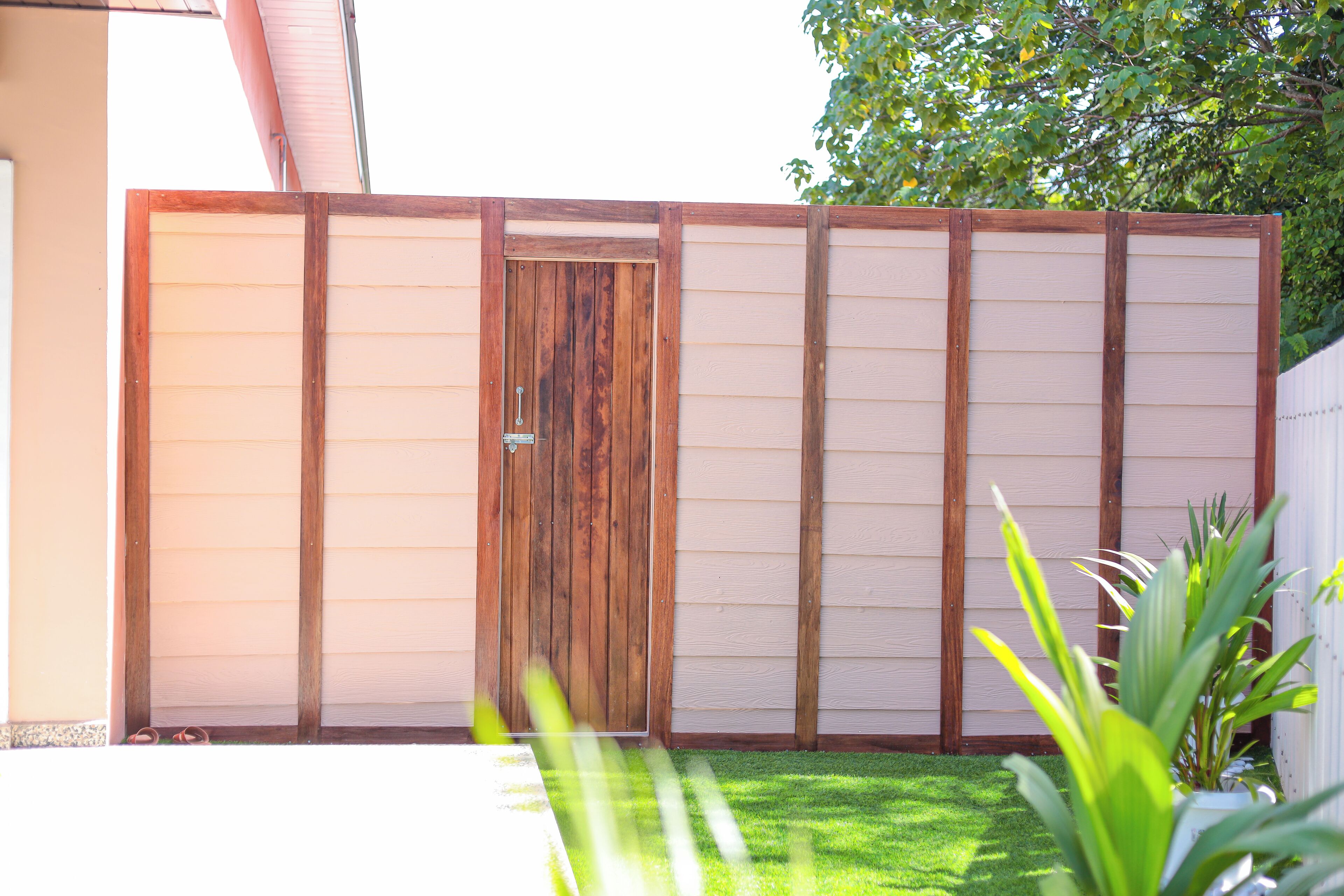 A wooden gate with a metal handle, a white fence, and a green lawn.