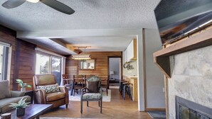 A cozy living room with a fireplace, wooden walls, and a dining area with a chandelier. - Pet Friendly, Short Walk to Lifts, Hot tub AN202 (Copper Mountain)