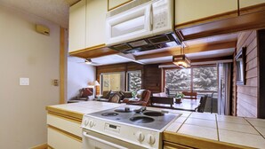 A compact kitchen with a stove, cabinets, and a dining area with a table and chairs. - Pet Friendly, Short Walk to Lifts, Hot tub AN202 (Copper Mountain)