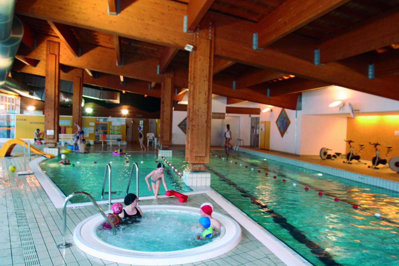 An indoor swimming pool with multiple lanes, a hot tub, and exercise bikes.