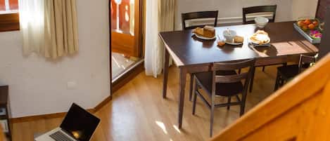 Un coin repas avec une table et des chaises en bois, un ordinateur portable posé sur une petite table, et un escalier menant à un autre niveau.