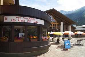 A restaurant named "VVF Villages Les Rives de l'Arc" with outdoor seating and mountain views.