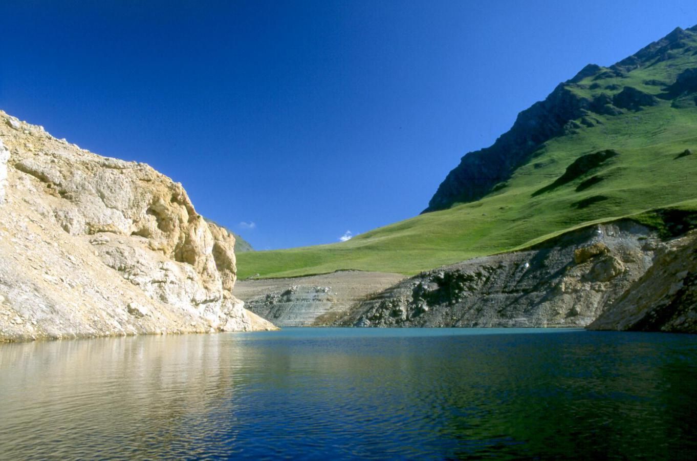 Ein ruhiger See, umgeben von felsigen Klippen und grünen Hügeln.