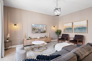 A modern living room with a sofa, two chairs, a round coffee table, a TV, and artwork on the wall. - Gorgeous 6-bedroom House With Private Pool (Davenport)