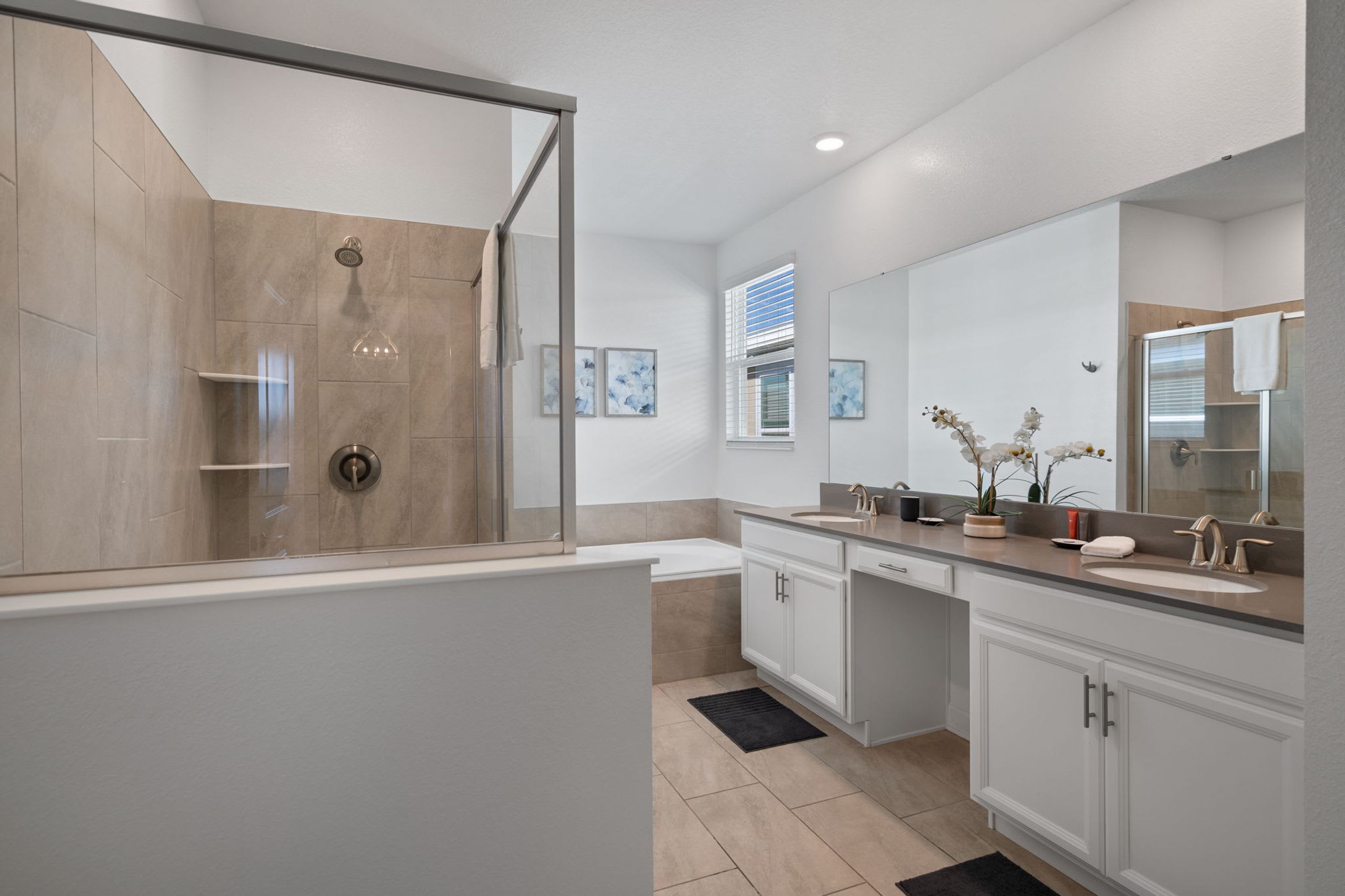 Une salle de bain moderne dotée d’une douche à parois de verre, d’un grand miroir et d’un meuble-lavabo avec un évier et un plan de travail.