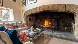 Una sala de estar acogedora con chimenea de piedra, un sofá con cojines estampados y una mesa de centro con libros y objetos decorativos.