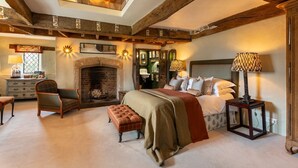 Un dormitorio acogedor con vigas de madera a la vista, una chimenea, una cama con manta roja y un tragaluz.
