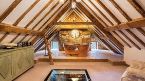 Habitación en ático con vigas de madera a la vista, una bañera de cobre grande, un reloj y una mesa de centro de vidrio.