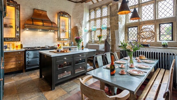 Una cocina con una isla central, armarios de madera y un comedor con una mesa dispuesta para cuatro.