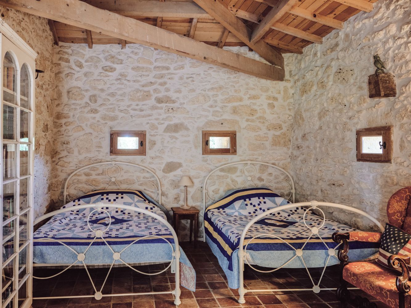 A rustic room with two metal beds, stone walls, and a wooden ceiling.