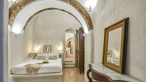 Een slaapkamer met een bed, een kaptafel met spiegel en een boogvormige deuropening naar een andere kamer.
