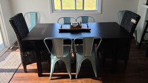 A dining area with a dark wooden table, four chairs, a window with a view of a park, and two framed pictures on the walls.