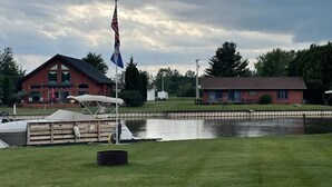 A building with a red roof, a dock with a boat, and a calm water body in front.
