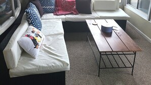 A room with a large window, a sofa with patterned cushions, a small table, and a carpeted floor.