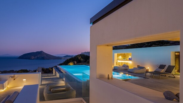 Una piscina infinita moderna con vista al mar y una montaña al atardecer.