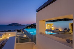 A modern infinity pool with a view of the sea and a mountain at dusk.