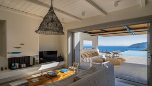 Una sala de estar moderna con televisor, sofá y comedor, con vistas a un paisaje marino.