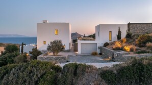 Una villa moderna con un muro de piedra, un garaje y vistas al mar.