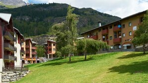 A hotel with multiple balconies, a grassy courtyard, and a mountainous backdrop. - Wifi, 300m from shops, parking, tv, ski locker, 35m², Val Cenis (Val Cenis)