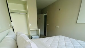 A hotel room with a large bed, white bedding, a wardrobe, and a desk with a computer. - Kleinville Marquês (Sao Leopoldo)