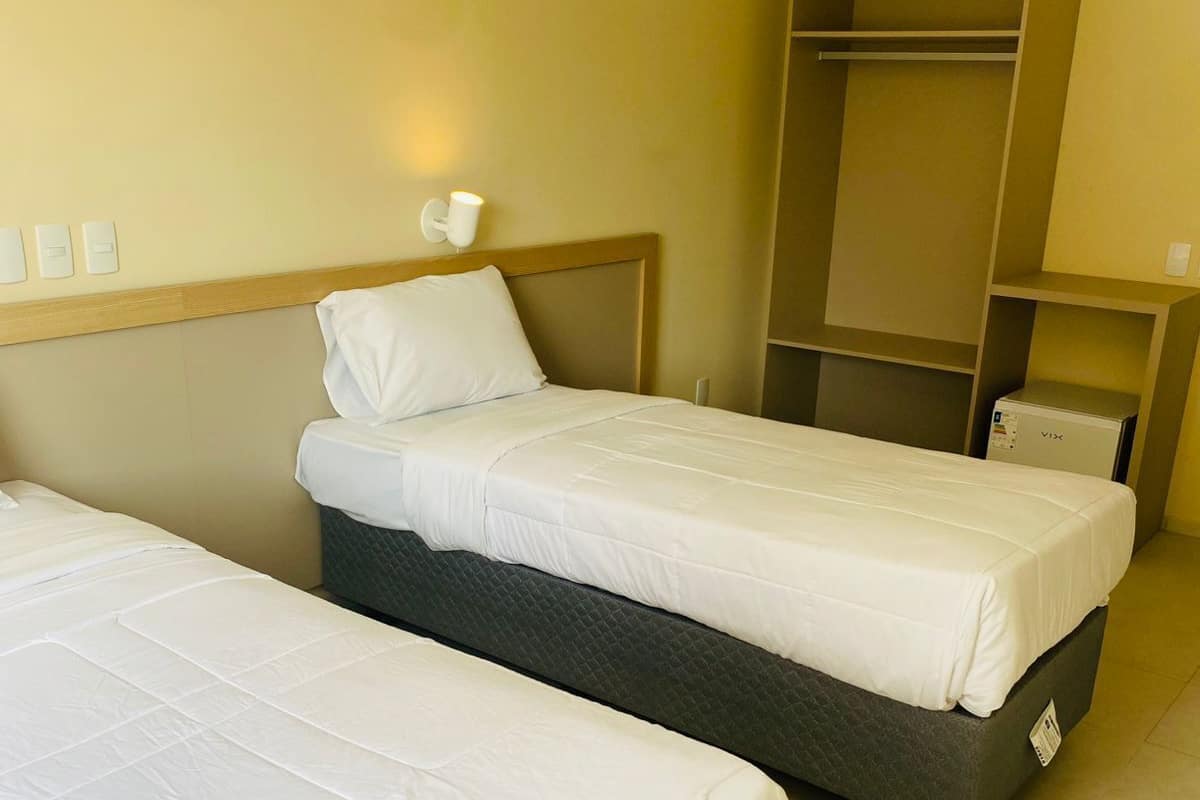 Hotellihuone, jossa on kaksi erillistä sänkyä, vaatekaappi ja yöpöytä, jossa on lamppu.
