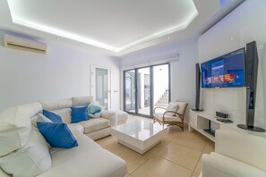 A modern living room with a white sofa, a coffee table, and a TV on a stand.