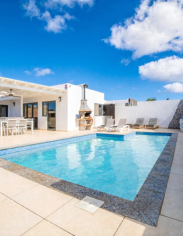 Une piscine avec des chaises longues, un espace barbecue et une pergola.