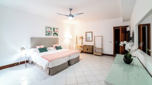 A bedroom with a bed, bedside tables, a ceiling fan, a dresser, a mirror, and a potted plant.