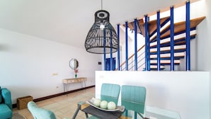 A modern living room with teal furniture, a glass dining table, and a staircase with blue railings.