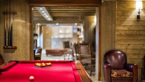 A pool table with balls, a pool cue, and a chair in a room with wooden walls and a visible fireplace. - 150m from ski slopes, swimming pool, balcony, tv, ski locker, 50-55m², Montchavin La Plagne (Bellentre)