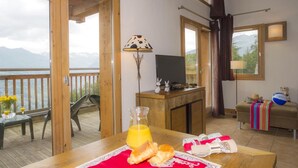 A room with a wooden table set for breakfast, a TV on a wooden cabinet, and a balcony with a view of mountains. - 150m from ski slopes, swimming pool, balcony, tv, ski locker, 50-55m², Montchavin La Plagne (Bellentre)