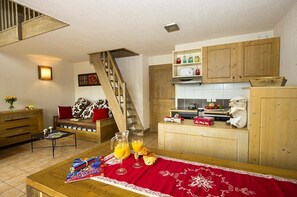 Un salon chaleureux avec un escalier en bois, une cuisine dotée de meubles en bois et un coin repas avec une nappe rouge.