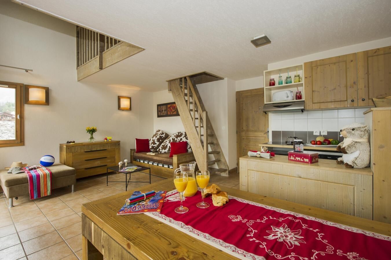 Een gezellige kamer met een houten ontbijttafel, een bank met een rode plaid, een trap en een keuken met houten kasten.
