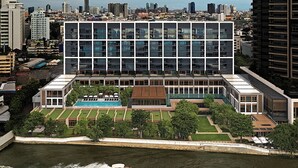 Een modern hotel met een dakterraszwembad, omringd door groen en uitzicht op het water.