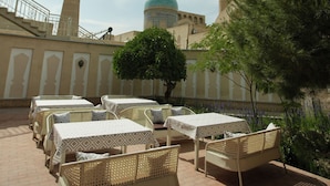 A terrace with outdoor seating, a view of a mosque with a dome, and a minaret. - Zargaron Boutique Hotel (Bukhara)