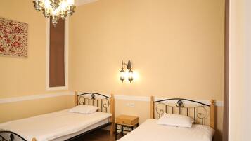 A room with two single beds, a small wooden nightstand, a wall-mounted light fixture, and a decorative wall piece.