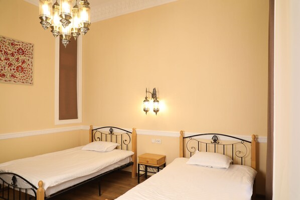 A room with two single beds, a small wooden nightstand, a wall-mounted light fixture, and a decorative wall piece.