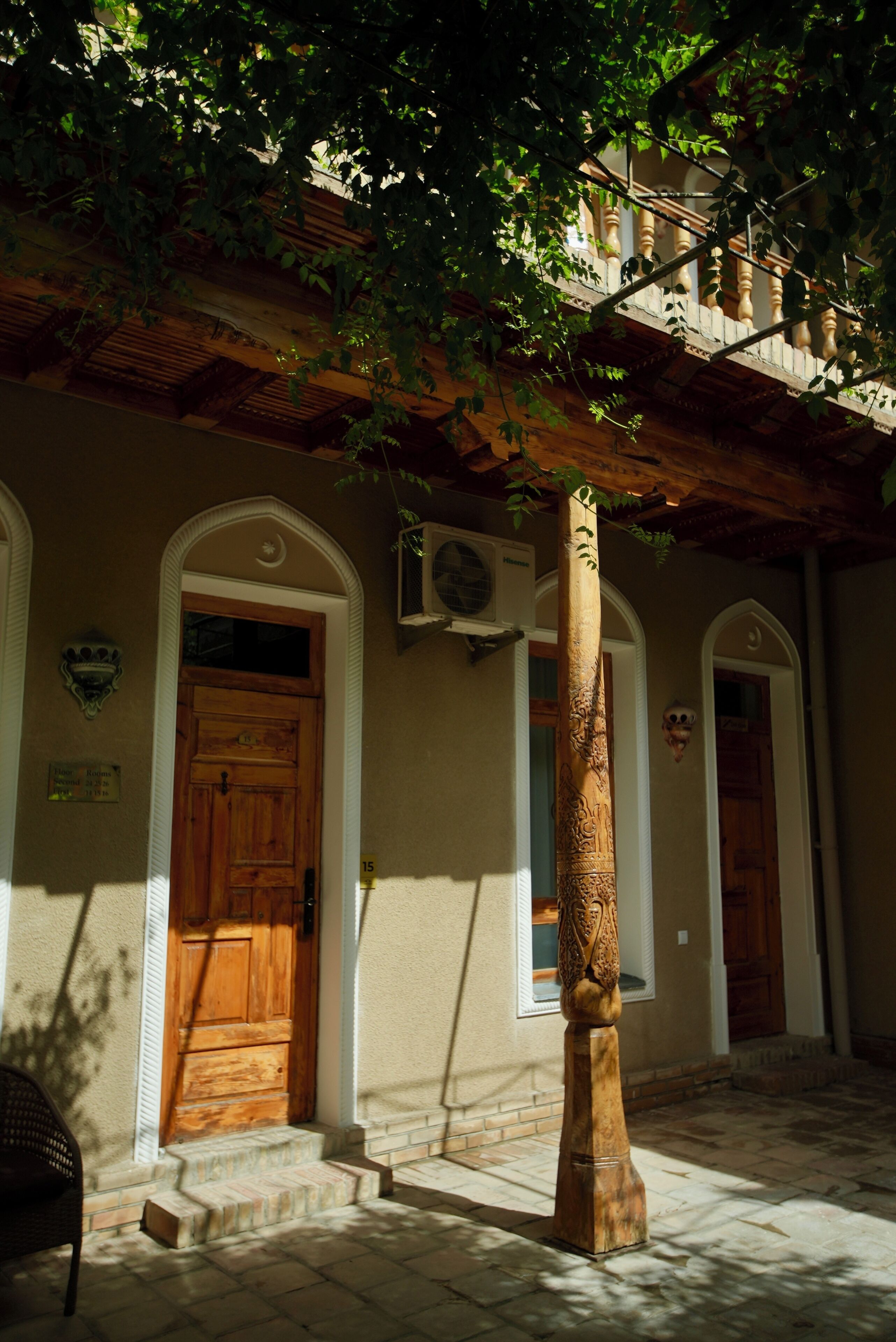 A courtyard with a wooden door, a column, and a staircase leading to an upper level.