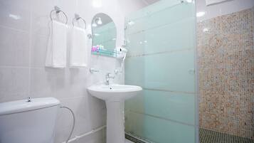 A modern bathroom with a white toilet, a pedestal sink, a glass shower enclosure, and a tiled shower wall.